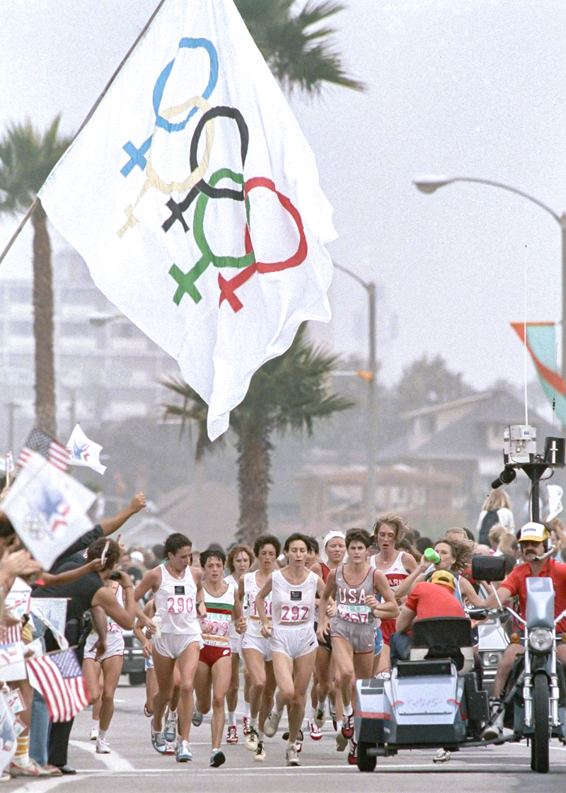 1984年洛杉磯奧運，女子馬拉松首次成為正式比賽項目，在8月5日的路跑賽程中有民眾揮舞奧運平權旗幟為女性選手加油。（攝影／Lennox McLendon／AP Photo／達志影像）